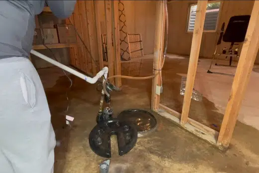 Sump pump basin and pump components being fitted near a foundation related to Mayflower Village neighborhood